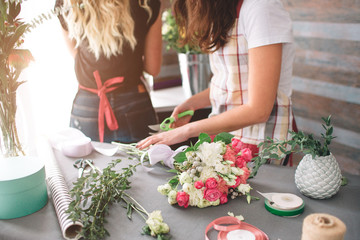Flowers delivery top view. Florists creating order, making rose bouquet in flower shop. Two female florists are doing bouquets. One woman collecting roses for a bunch, another girl is working too.