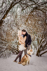 Sweet couple with dog standing by a tree in a snowy park