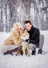 Fototapeta na wymiar A pretty couple walks with their dog in a snowy park