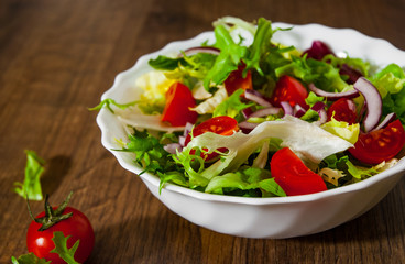 various fresh mix salad leaves with tomato in bowl on wooden background