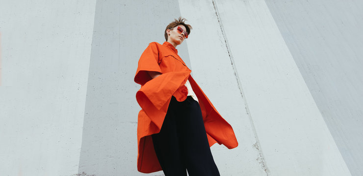 Alternative stylish young female on orange/red coat on street/minimalist composition.