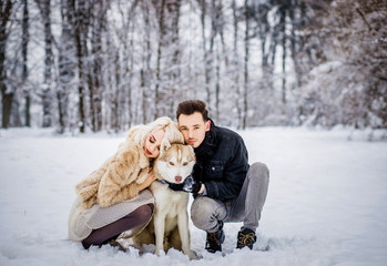Fototapeta na wymiar A magic couple walks with their dog in a snowy park
