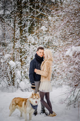 The charming couple walks with their dog in a snowy park