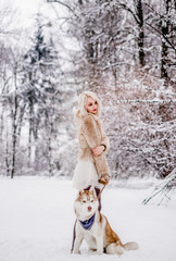 A beautiful girl stands with her dog in the winter forest