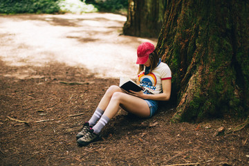 Woman reading a book sitting near a big sequoia tree.