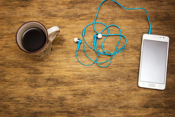 A cup of coffee with a phone and headphones on the table