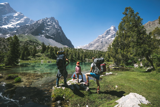 family with mountaineering and camping equipment standing in front of crystal clear lake in alpine mountain landscape
