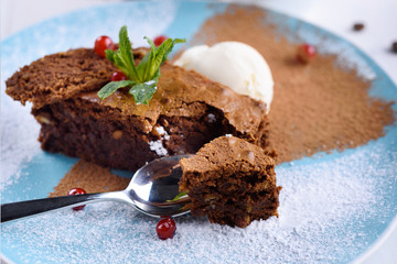 Tasty chocolate cake with ice cream, mint and berries on plate on the table on light background, close-up. Chocolate brownie