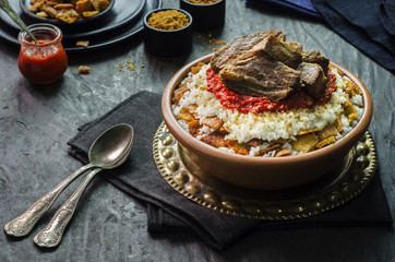 Arabic cuisine, Egyptian oriental Fettah with white rice and crispy bread topped with seasoned garlic red sauce,crispy fried garlic and veal chunks on rustic dark background.