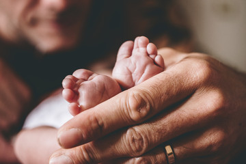 A father holds the small feet of his newborn baby