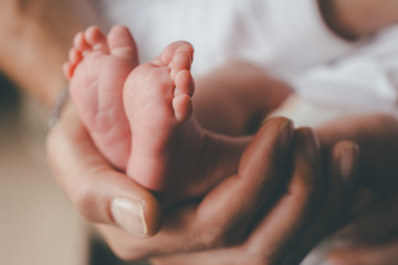 small feet of a newborn supported by the hand of his father - obrazy, fototapety, plakaty
