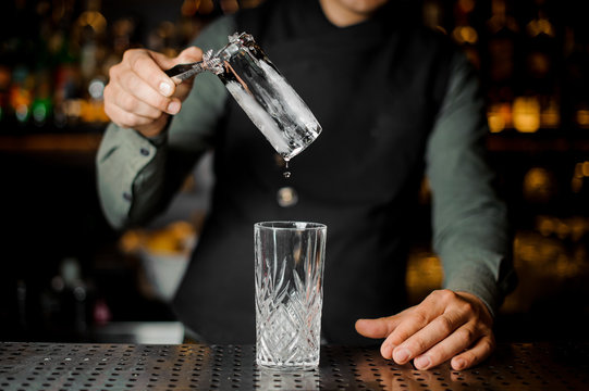 Bartender putting a big ice cube into an empty glass