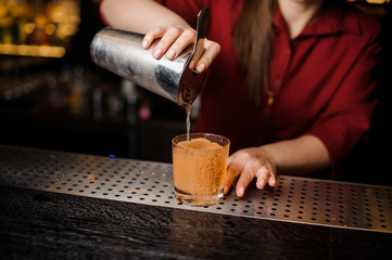 Fototapeta na wymiar Bartender girl filling cocktail glass at the bar counter