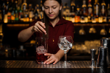 Bartender girl stiring a fresh light red cocktail