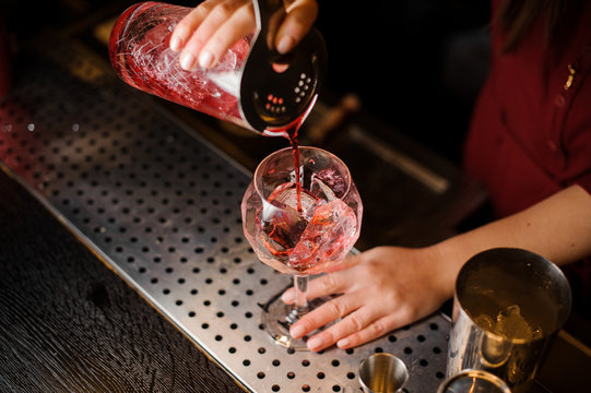 Bartender girl pouring a liquid red cocktail into the glass