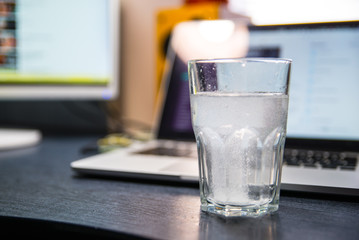 glass of water with aspirin. laptop on background. overloaded with office work