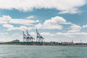 Beautiful seascape. Azure wavy restless sea with splashes and foam on background a cloudy blue sky on the horizon industrial large seaport on the shoreline