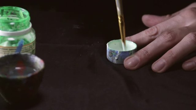 Close up shot of paint jar and paintor hand with paintbrush mix paints.