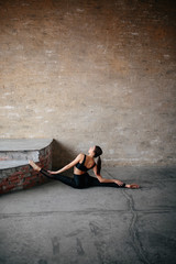 Portrait of a young woman working on a gray wall background, practice yoga and Pilates exercises to do the splits.