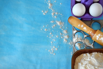 Eggs, flour and kitchen utensils for cooking homemade dumplings on blue background. Copy space