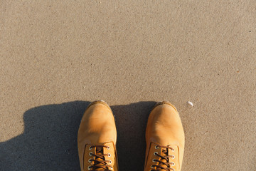 Close up Legs in brown pastel shoes with laces stand on the beach with wet sand near the sea