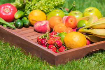 Various vegetables and fruits on a wooden tray against a background of green grass