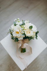 Close up A beautiful tender bridal bouquet in pastel colors of roses, peonies and green twigs tied with a long silk beige ribbon on background a wooden chair. Wedding accessories for bride