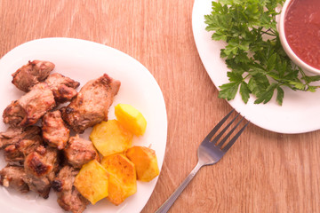 Mutton shish kebabs on two skewers with baked potato on the plate with fork on the wooden table