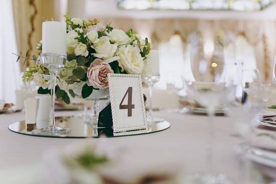 Beautiful decoration of a wedding banquet in a restaurant in pastel colors. Decoration of banquet dinner table vase with flower arrangement, candlestick, card with number of table in frame