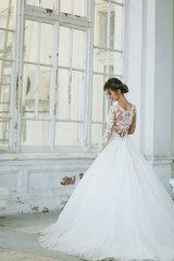 Obraz premium Beautiful wedding photosession. Young bride in a white lace dress with a long plume with an exquisite hairstyle in vintage interior on the veranda of an old house with columns near the garden