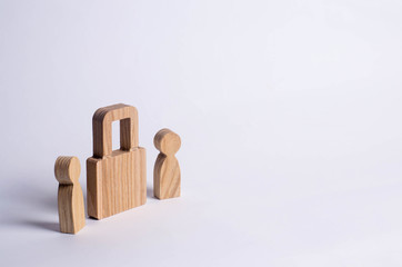 Two people stand near a padlock and keep secrets, information, entrance. Wooden figures of persons carry guards from wicked men, spies. The concept of the preservation of secrets, information.