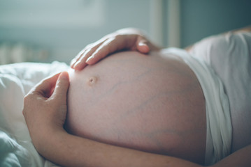 Pregnant woman cuddling belly in bedroom at home