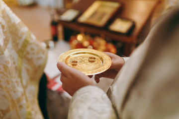 Wedding in the Orthodox Church. Golden patterned saucer with wedding rings for the bride and groom in the hands of man against the background of the iconostasis and church interior