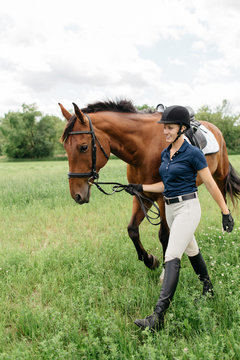 Young Female Horse Rider Leading Her Horse In A Field On Foot