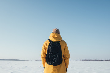 Alone traveler in yellow jacket with black backpack on snowy winter field