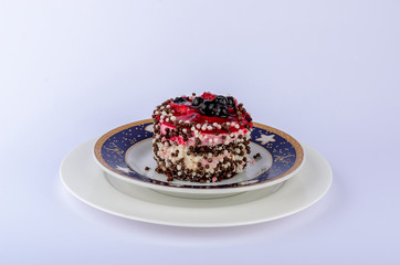 round cake with curd filling filled with red jelly and decorated with black currant, sprinkled with rice balls on two saucers white and with a blue stripe on the edge, place under the text