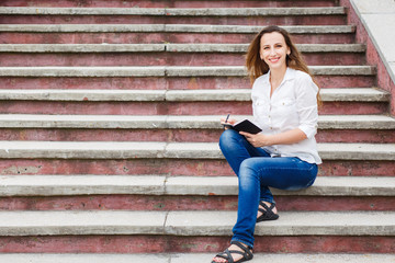 Young woman sitting on stairs and making notes in notebook