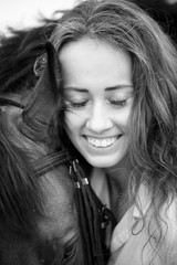 Young happy rider woman with her bay horse. Portrait of smiling girl with her stallion in paddock on summer day