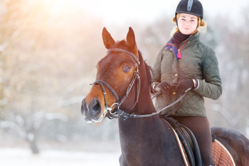 Obraz premium Young happy woman riding her bay horse on winter field. Winter equestrian activity background