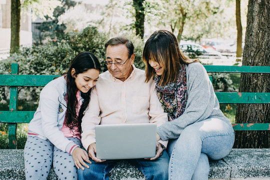 .A father with his daughters sitting on a stone bench, learning to use the laptop. Relaxed autumn day in family outdoors. Lifestyle portrait...