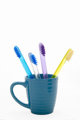 four multi-colored toothbrushes in a blue glass