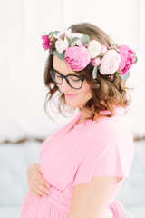 Young beautiful pregnant girl in a pink dress on a white background near a vintage sofa