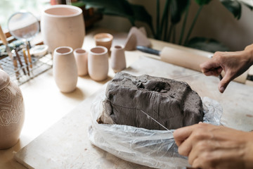 female ceramics maker pulling slice of clay from larger piece to begin new project