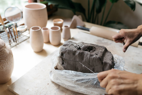 female ceramics maker pulling slice of clay from larger piece to begin new project