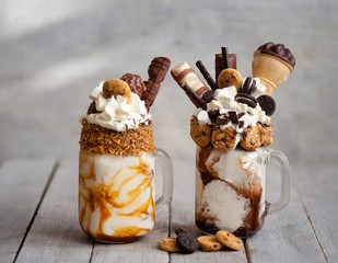  Caramel and chocolate indulgent exreme milkshakes with chocolate cake, oreo, marshmallow and sweets. Crazy freakshake food trend. Copy space, ice cream in a cube, 