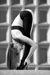 Black and white photo of woman in sports bra and high heeled boots doing a forward fold