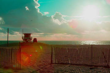 Sun flare across a scene of a lifeguard stand at the beach with puffy clouds