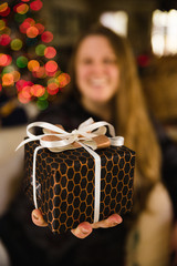 Woman holds beautifully wrapped present with Christmas tree lights in the background