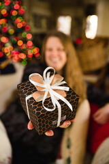 Woman holds beautifully wrapped present with Christmas tree lights in the background