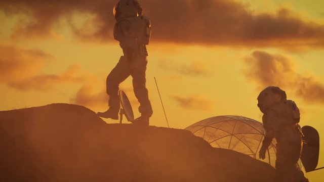 Two Silhouettes of the Astronauts Explore Red Rocky Alien Planet. In the Background Sunset with Base/ Research Station. Shot on RED EPIC-W 8K Helium Cinema Camera.